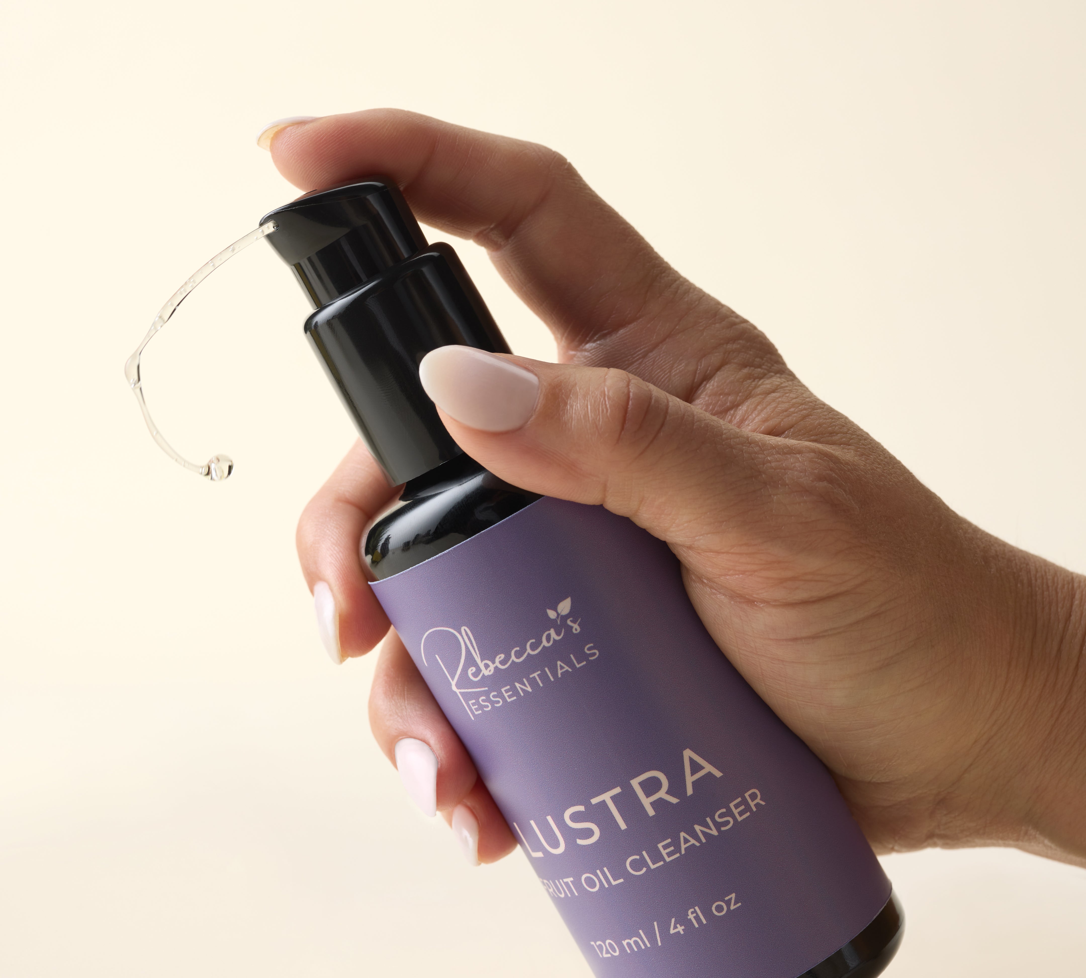 Hand holding a purple bottle labeled 'Lustra Fruit Oil Cleanser' against a beige background