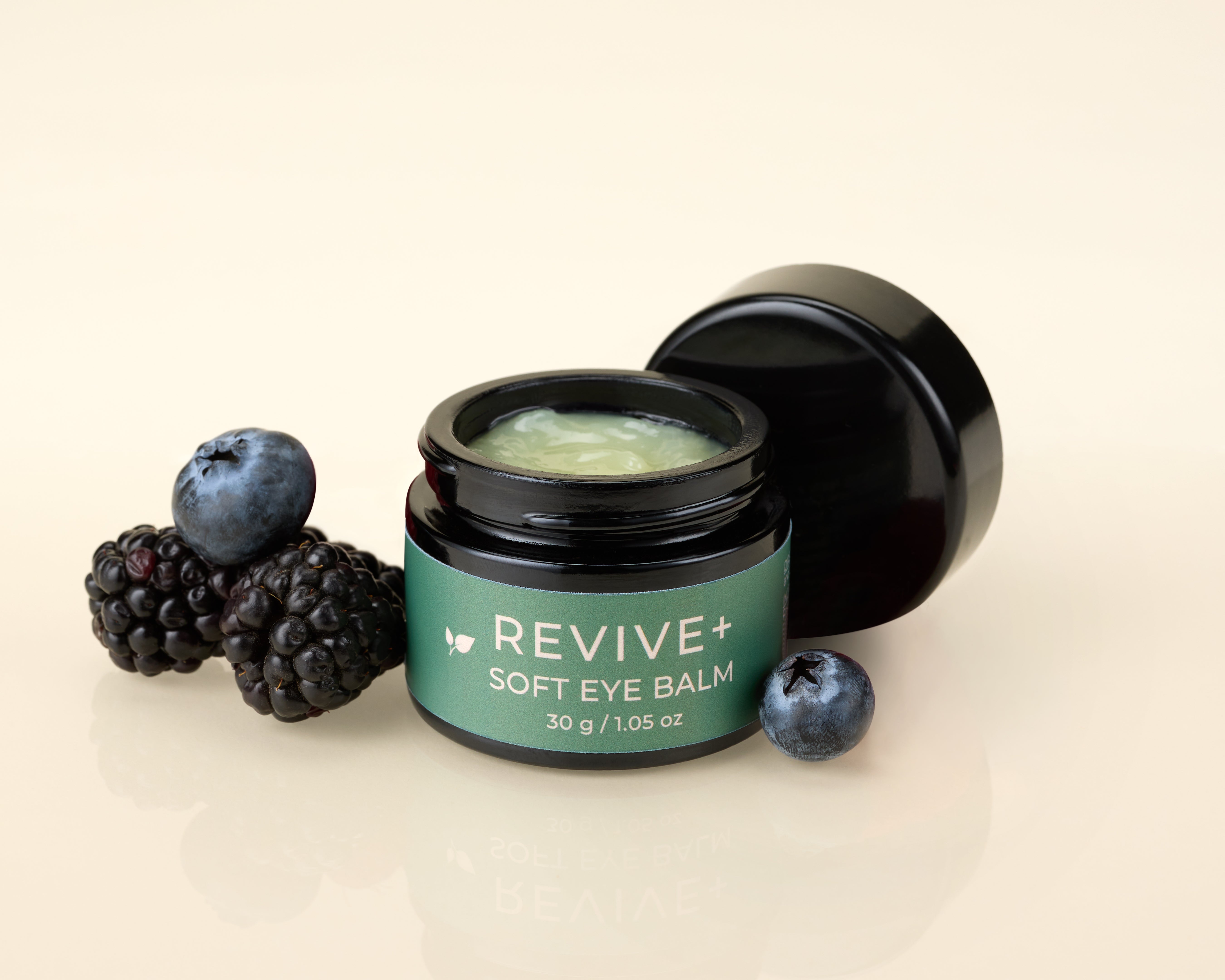 Revive+ soft eye balm jar with lid off and with berries on a beige background