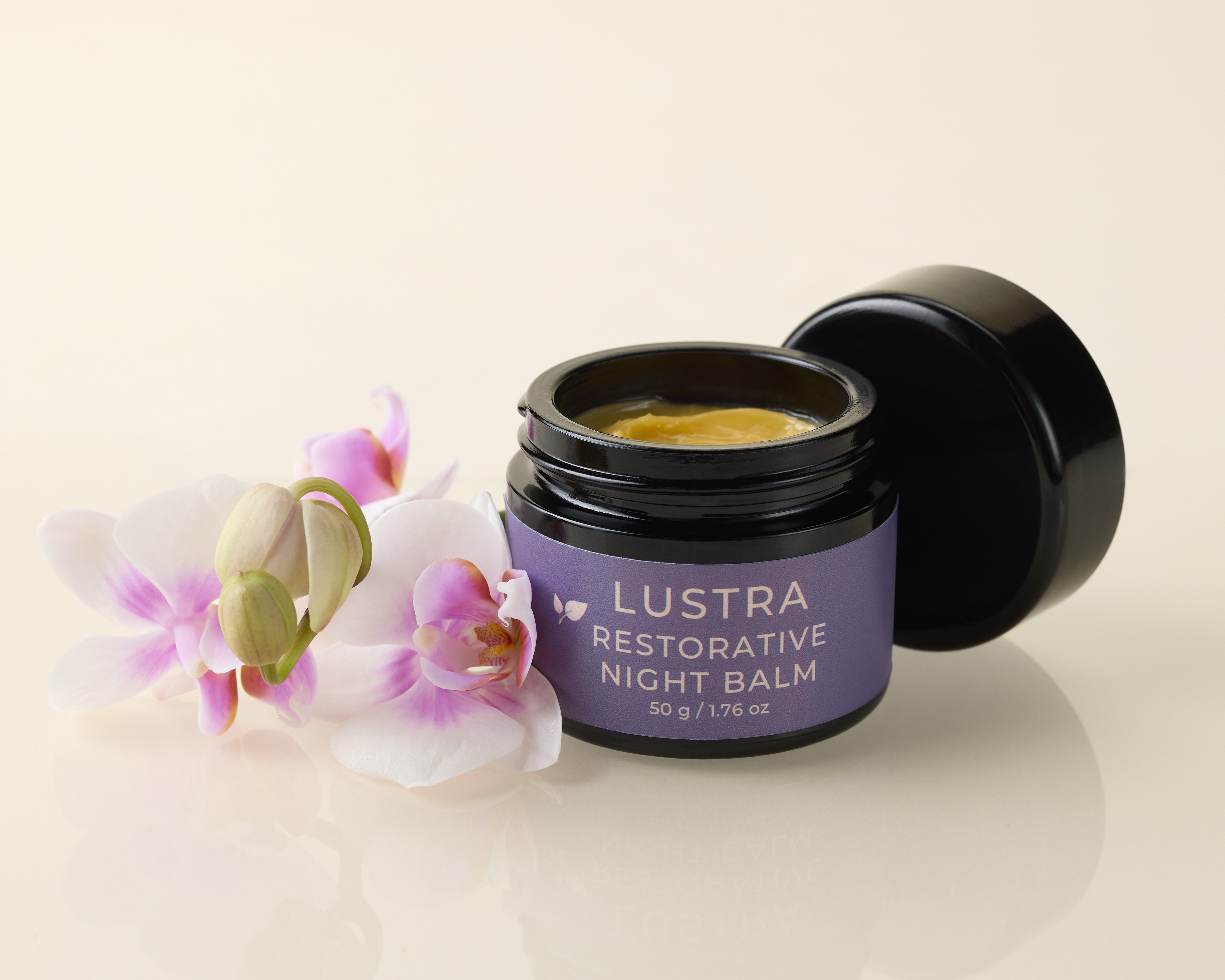 Lustra Restorative Night Balm jar with a black lid on a light background.  Lid is off and purple orchids next to jar.